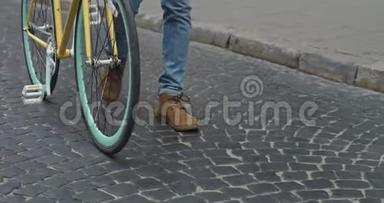 在现代黄薄轮胎自行车附近的旧石洞上行走的牛仔裤和休闲靴的特写镜头。 侧面